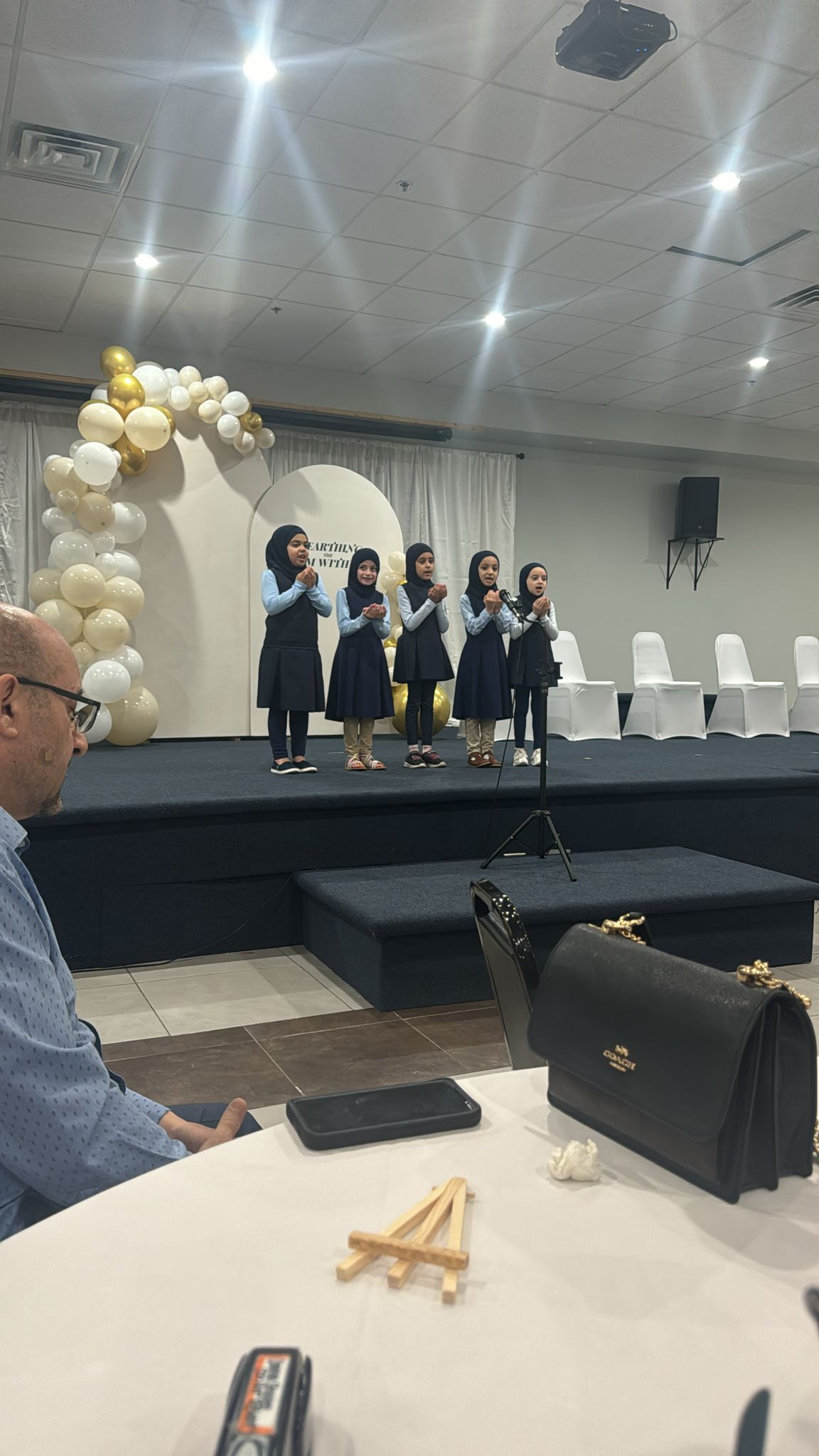 A Group of Children Sitting on Stage at a School Event, Smiling and Looking at the Audience.