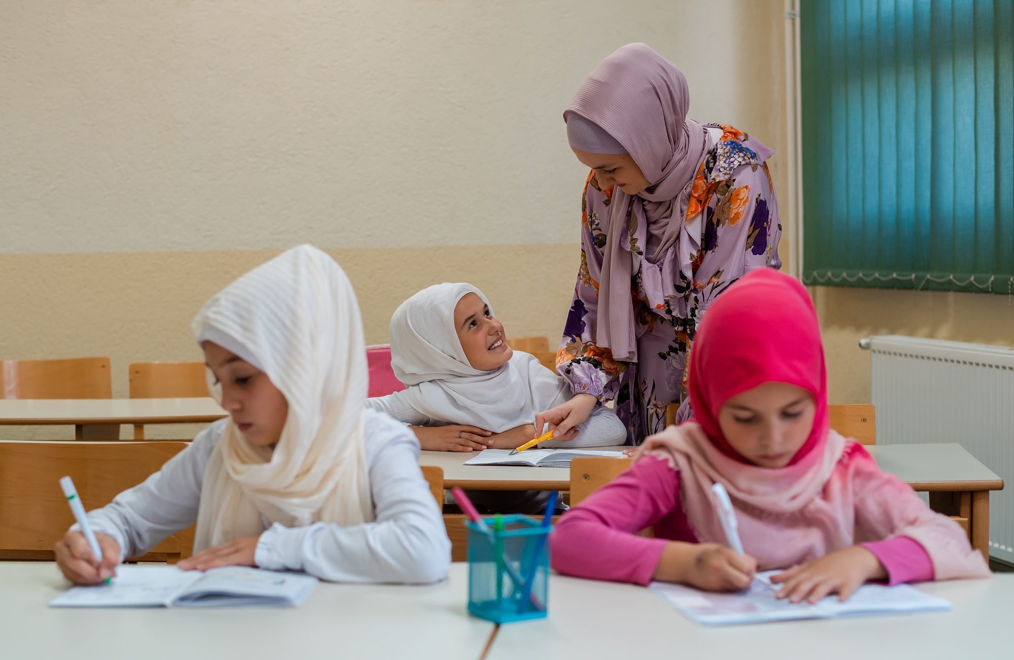 Female Hijab Muslim Teacher Helps School Children to Finish the Lesson in the Classroom.